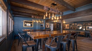 Um restaurante com um balcão de madeira comprido, diversas áreas de estar e teto rústico com vigas aparentes.