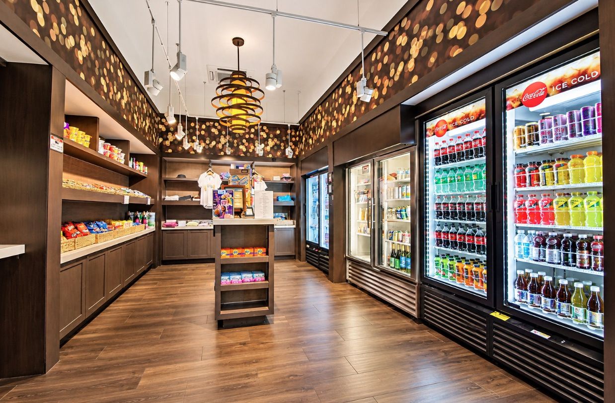 L’intérieur d’un magasin, avec des étagères remplies d’en-cas, un comptoir central et des présentoirs réfrigérés pour les boissons.