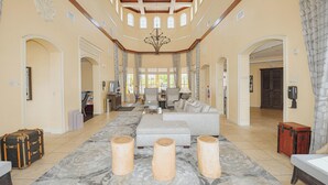 A spacious living area with a large sofa, ottoman, and wooden stools. There are multiple doors leading to other rooms, and a chandelier hangs from the ceiling. - WorldQuest Orlando Resort (Orlando)