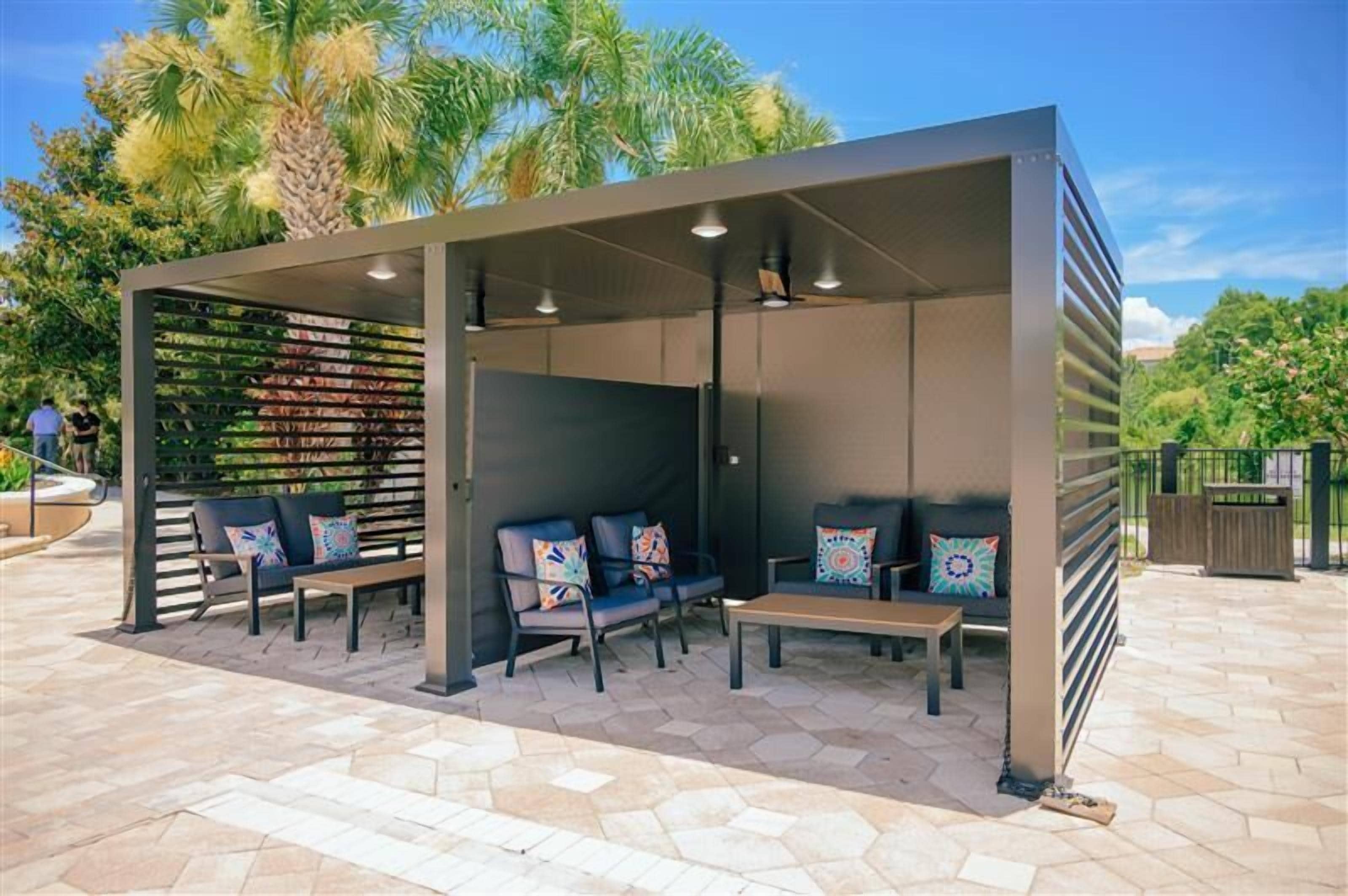 Un espacio al aire libre cubierto con varias sillas y una mesa, rodeado por una valla de madera y palmeras.