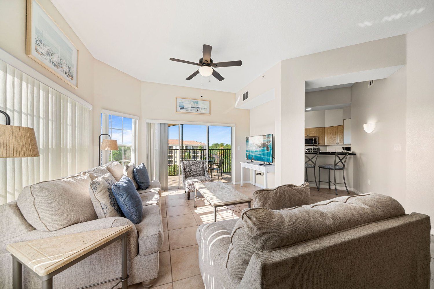 A spacious living area with a sofa, a coffee table, and a television. There is a balcony with a view of the outdoors.