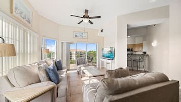 A spacious living area with a sofa, a coffee table, and a television. There is a balcony with a view of the outdoors.