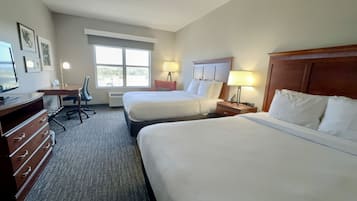 A hotel room with two beds, a desk, a chair, a TV, and a window.