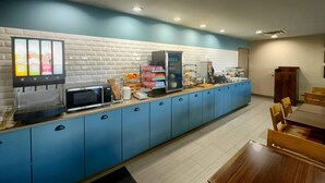 Uma cozinha compacta equipada com micro-ondas, cafeteira e dispensador de bebidas.