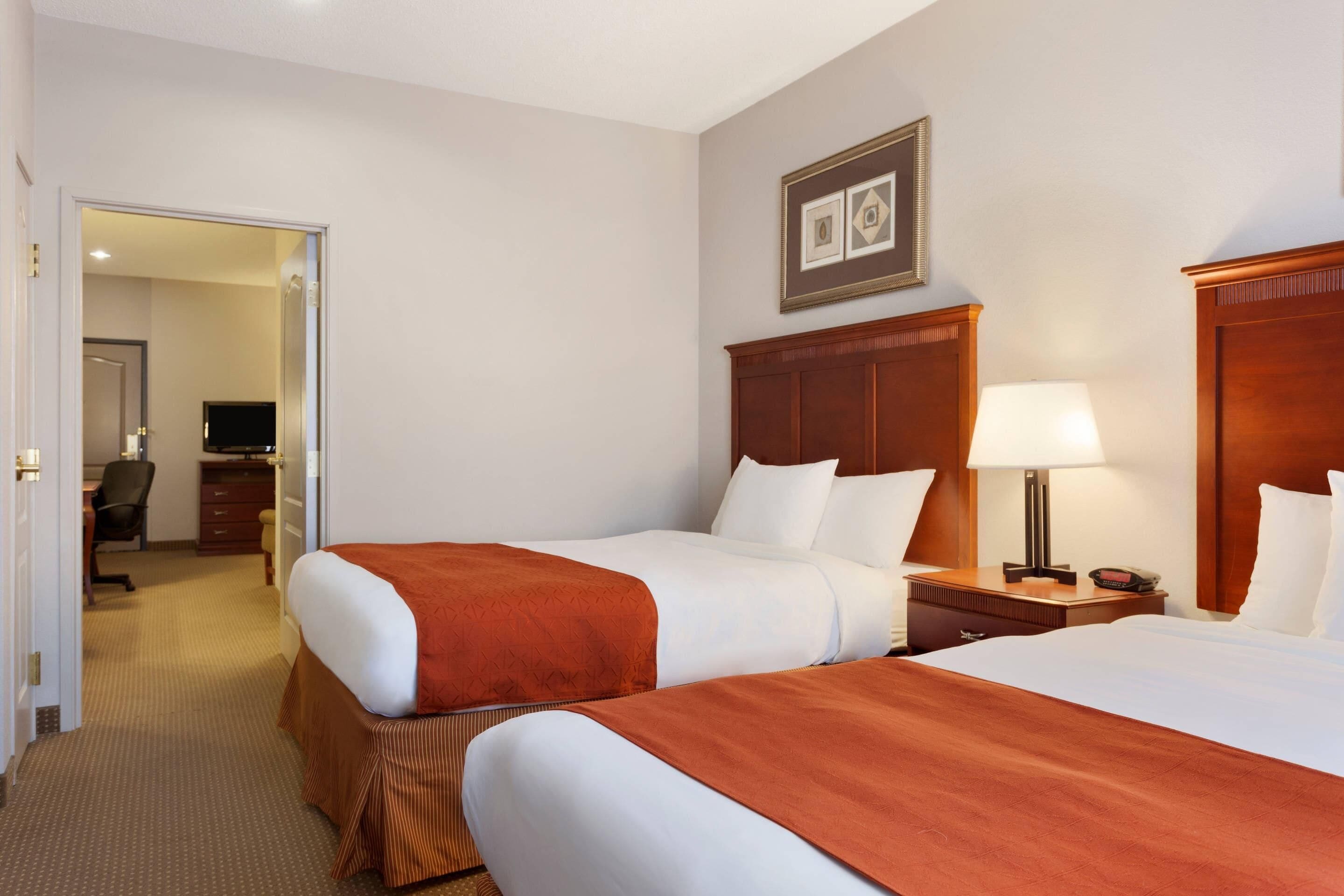 A hotel room with two beds, a desk, a chair, a TV, and a framed picture on the wall.