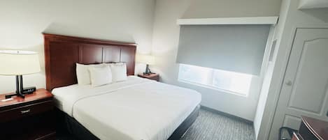 A hotel room with a large bed, two bedside tables with lamps, a window with a blind, and a door.