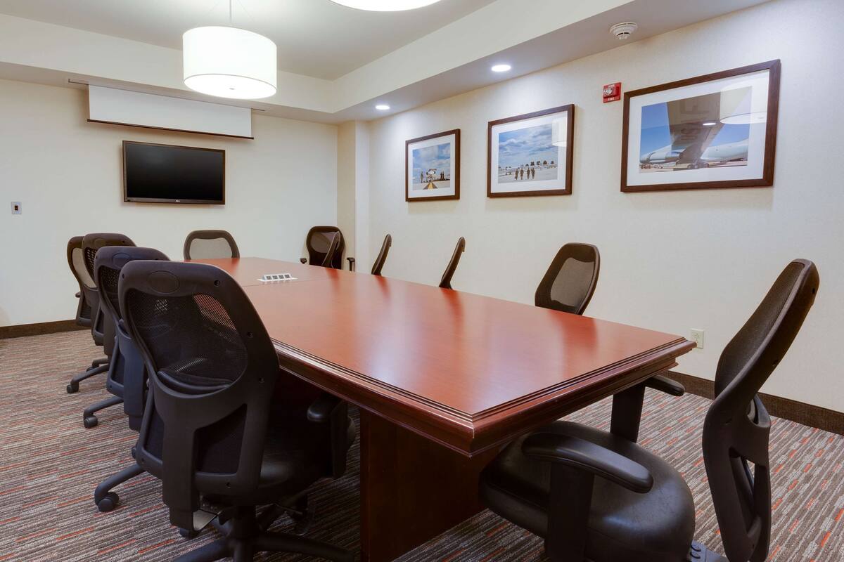 Une salle de conférence avec une longue table, six chaises, un téléviseur à écran plat et des tableaux encadrés accrochés aux murs.