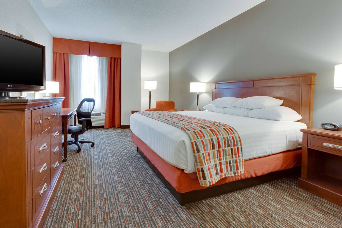 Une chambre d’hôtel avec un grand lit, un bureau avec une chaise, une télévision et deux lampes de chevet.