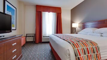 A hotel room with a bed, a TV, a desk, and a window with curtains.