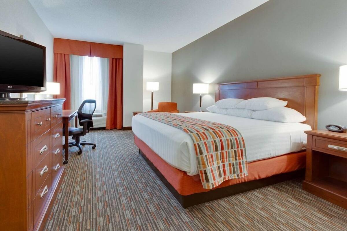 Une chambre d’hôtel comprenant un lit, un bureau avec une chaise, une télévision et une commode.