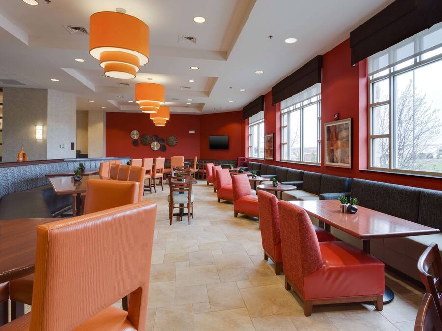 A spacious restaurant with high ceilings, orange pendant lights, and large windows offering a view of the outdoors.