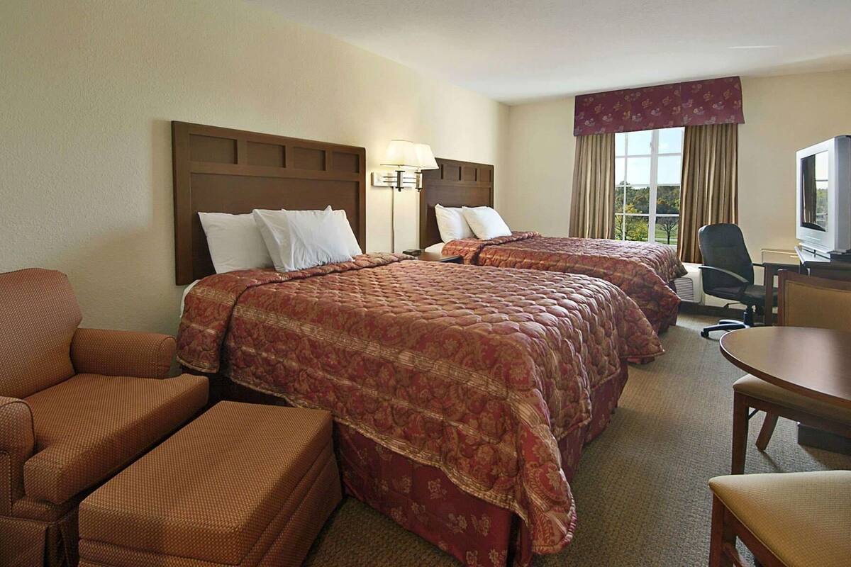 A hotel room with two beds, a desk, a chair, and a TV.