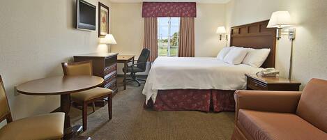 A hotel room with a bed, a desk with a chair, a sofa, a TV, and a window with curtains.
