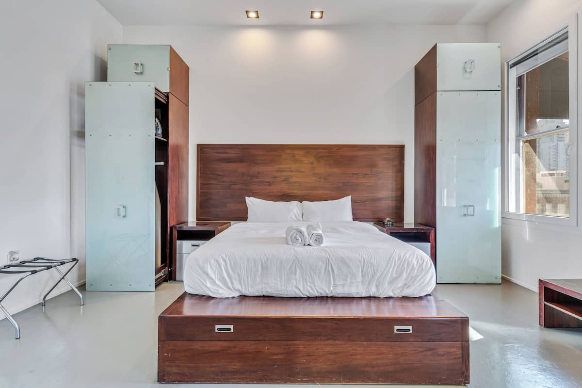 A modern bedroom with a large bed, wooden headboard, built-in wardrobes, and a window.