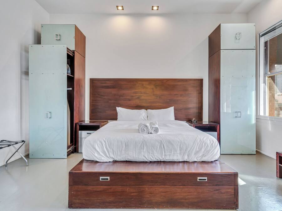 A modern bedroom with a large bed, wooden headboard, built-in wardrobes, and a window.