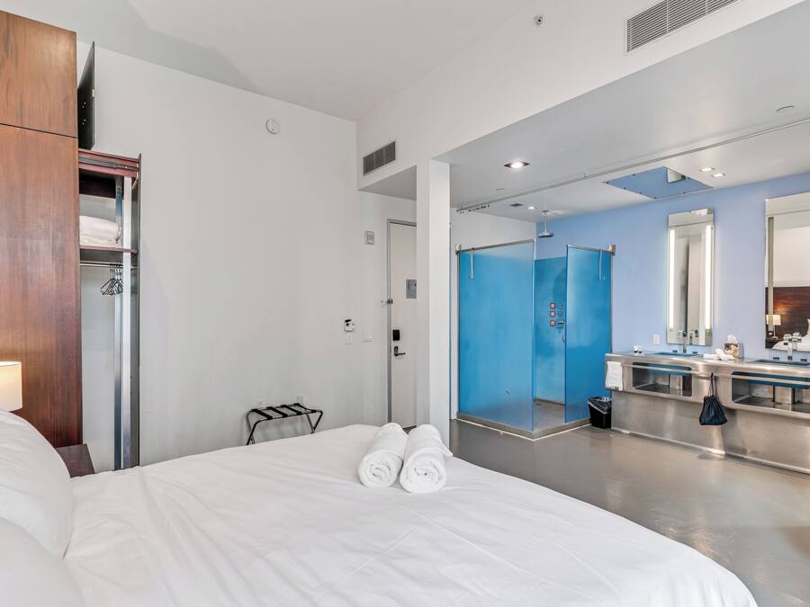 A hotel room with a bed, a wardrobe, a bathroom with a mirror, and a shower area.
