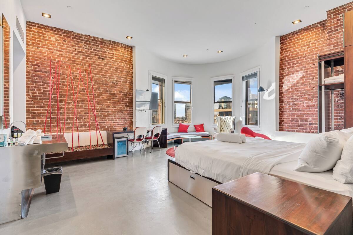 A modern bedroom with a brick wall, a bed, a desk, and a seating area.
