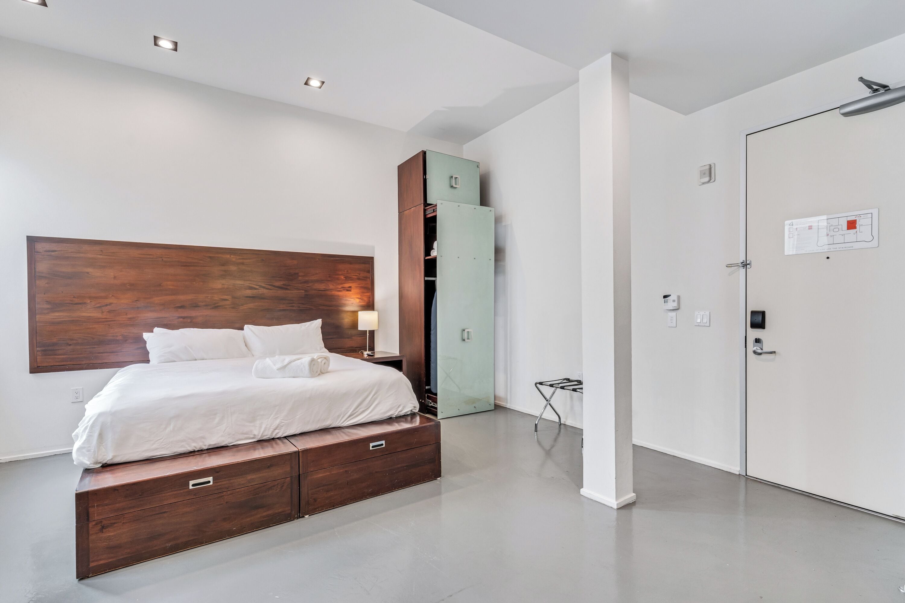 Un dormitorio moderno con cabecera de madera, cama con ropa de cama blanca, armario empotrado y mueble auxiliar.