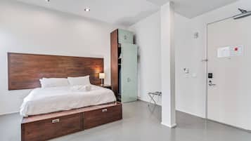 Un dormitorio moderno con cabecera de madera, cama con ropa de cama blanca, armario empotrado y mueble auxiliar.