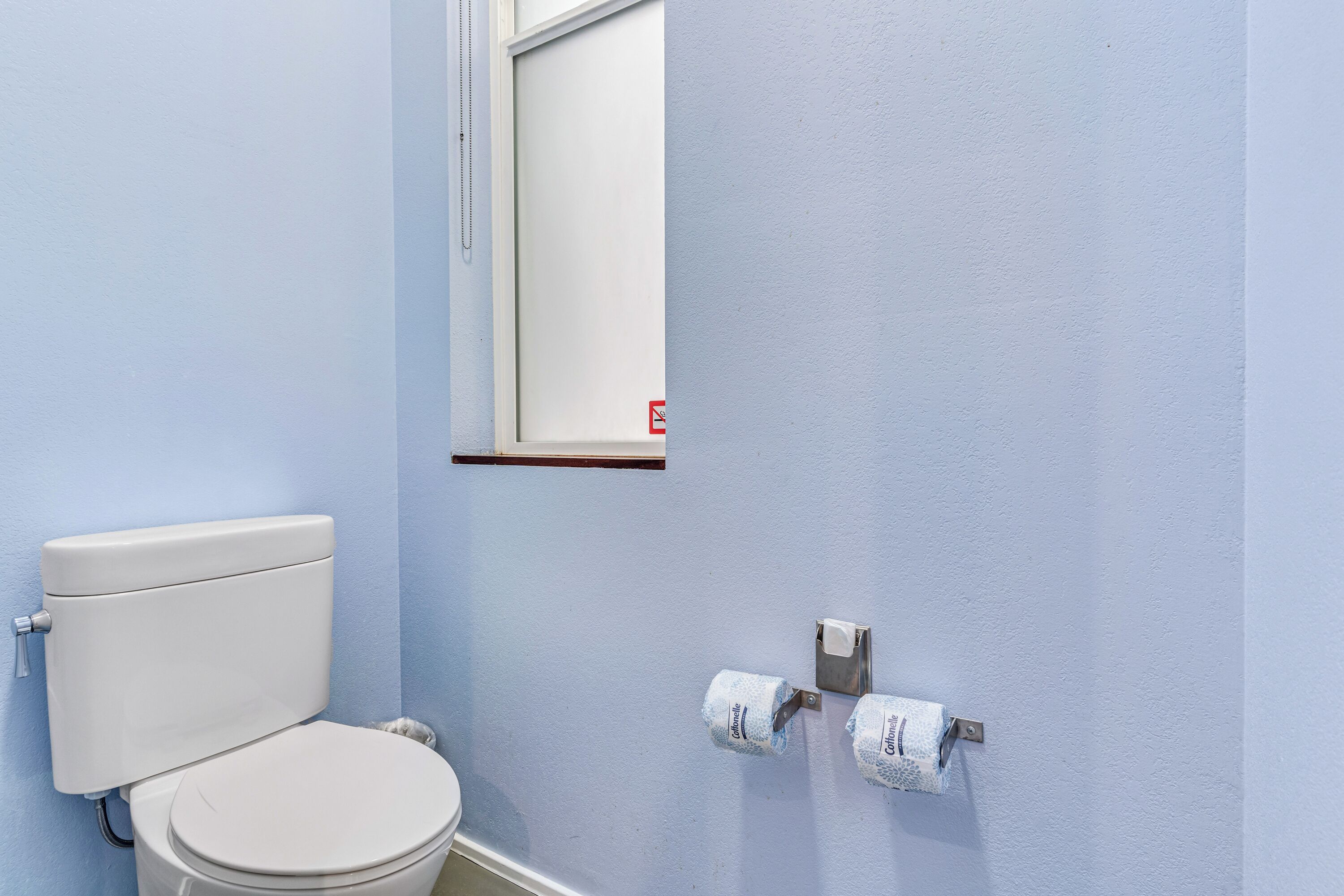 A bathroom with a toilet, a window, and two rolls of toilet paper on the wall.