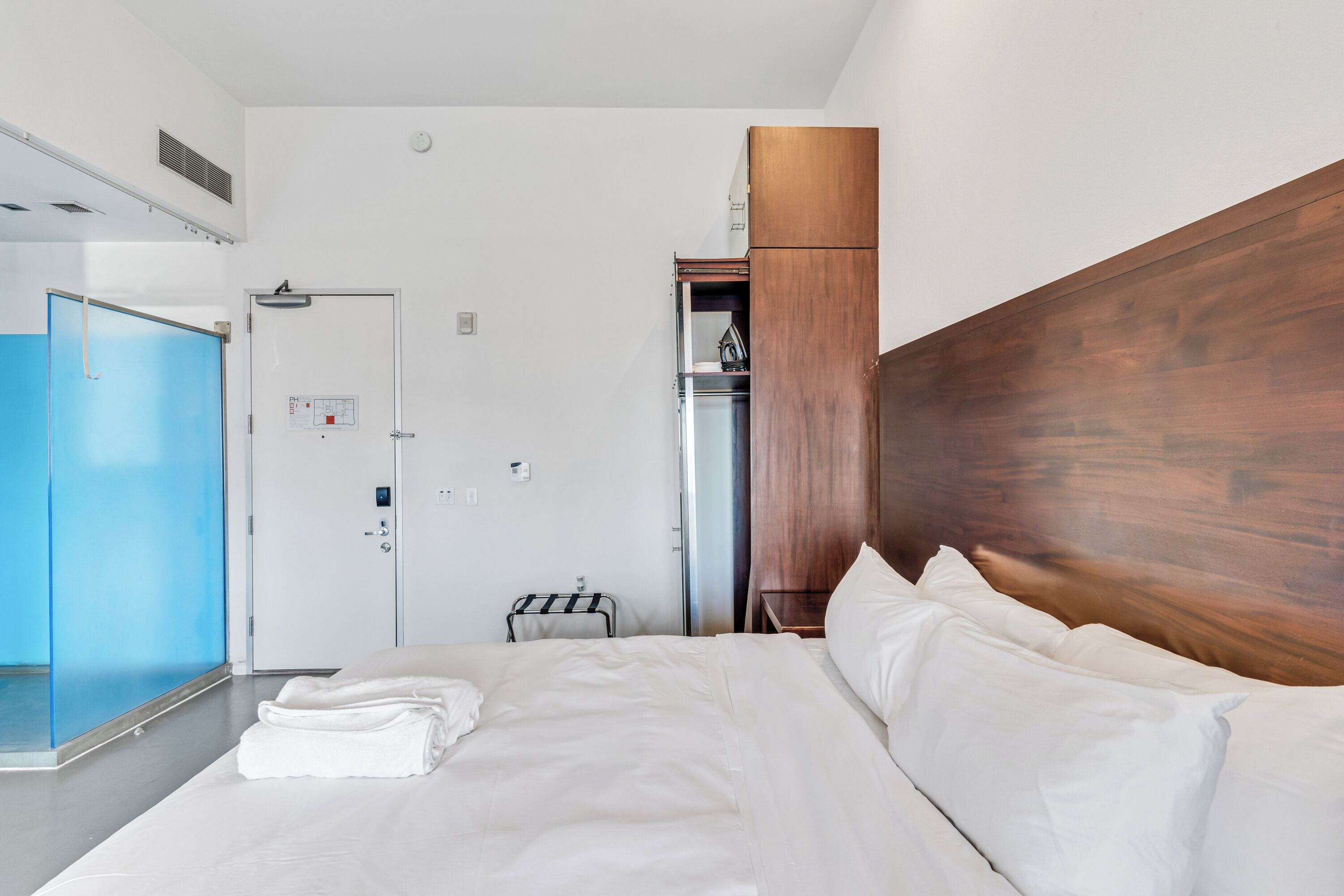 Hotellihuone, jossa on sänky, vaatekaappi, peili ja ovi.
