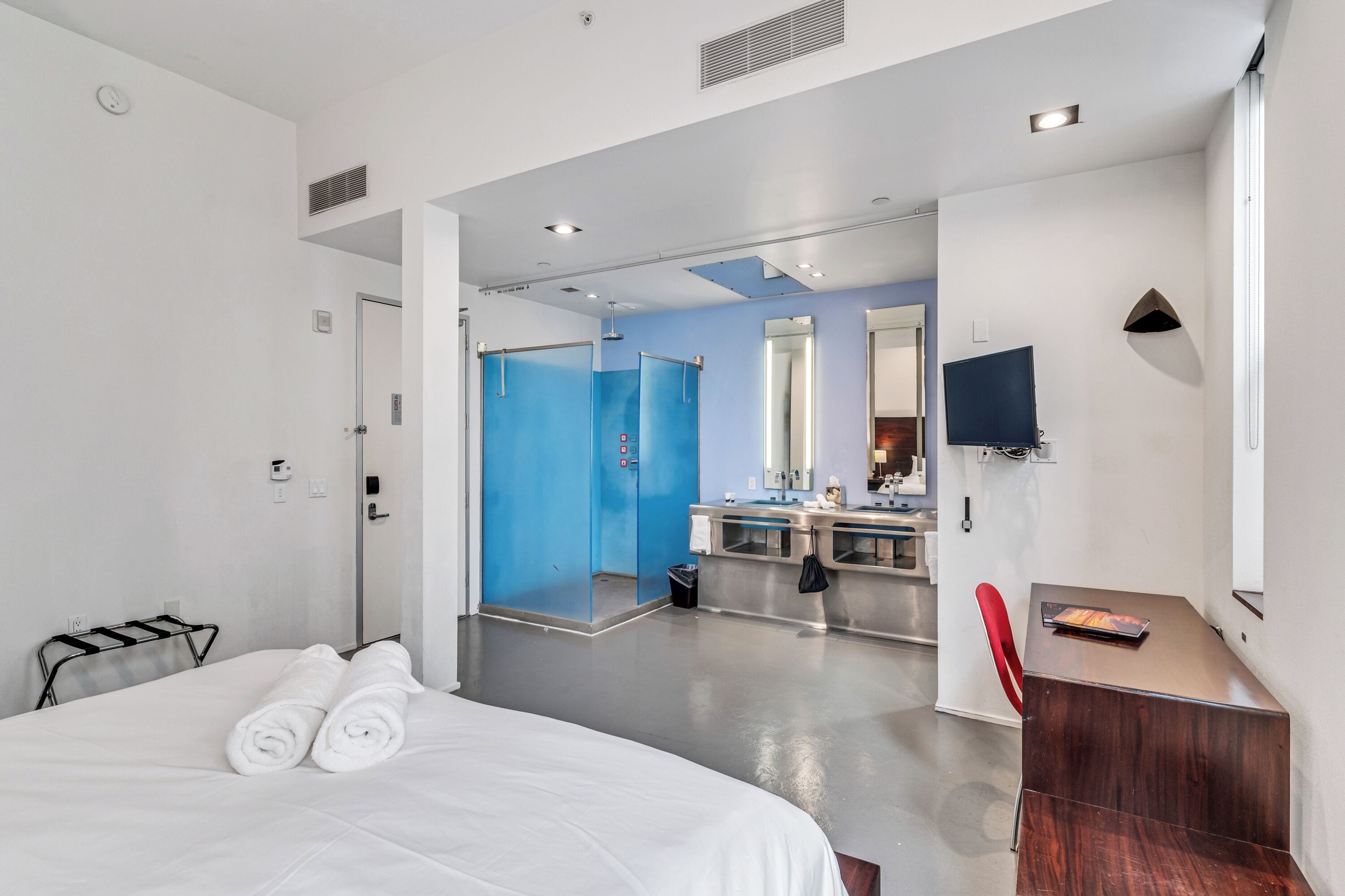 Une chambre d’hôtel moderne équipée d’un lit, d’un bureau, d’une chaise, d’une salle de bain avec un miroir et d’une télévision.