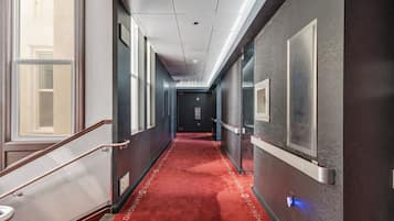 A hotel hallway with a red carpet, a staircase, and a door at the end.
