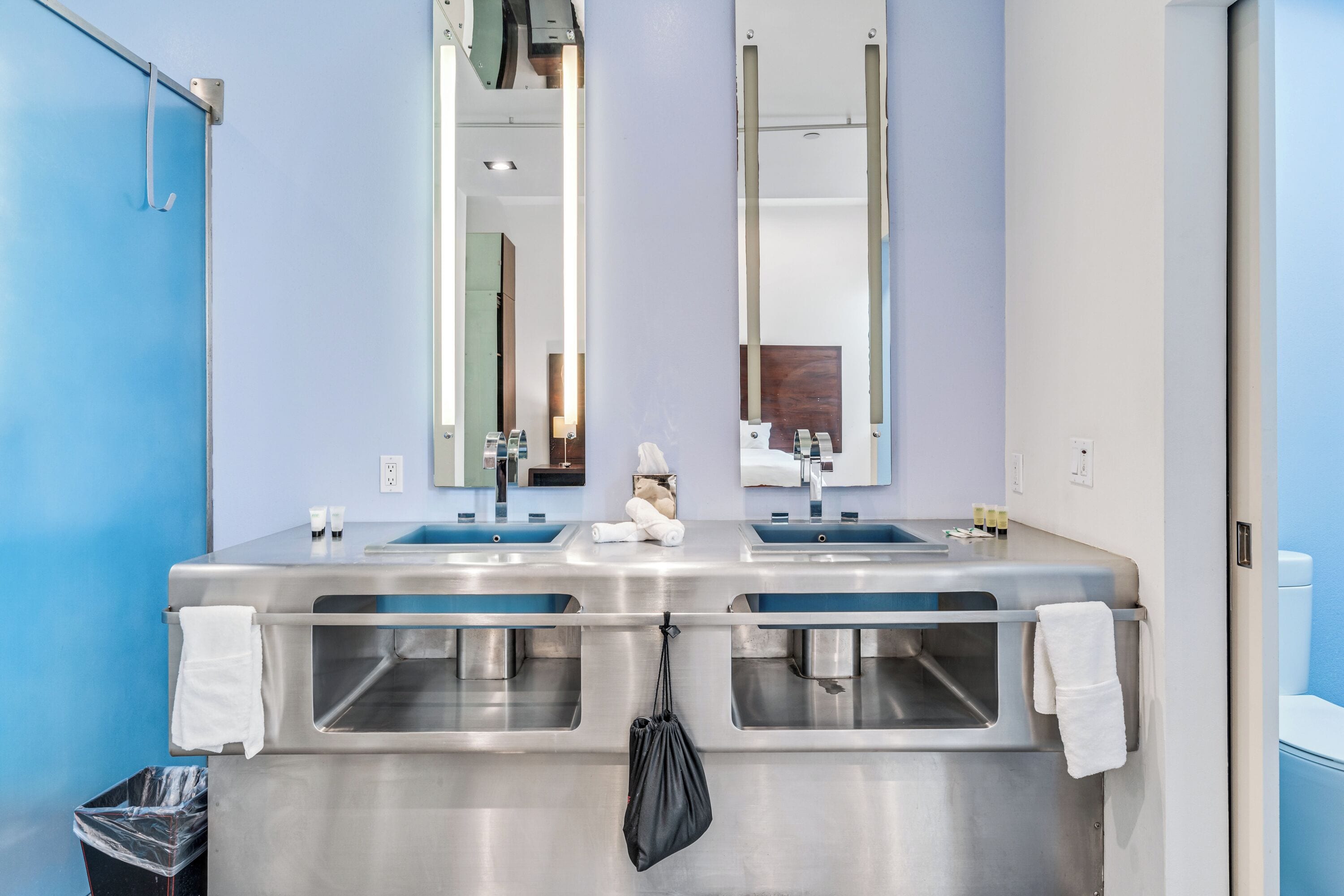 A bathroom with two sinks, a mirror, and a trash bin.