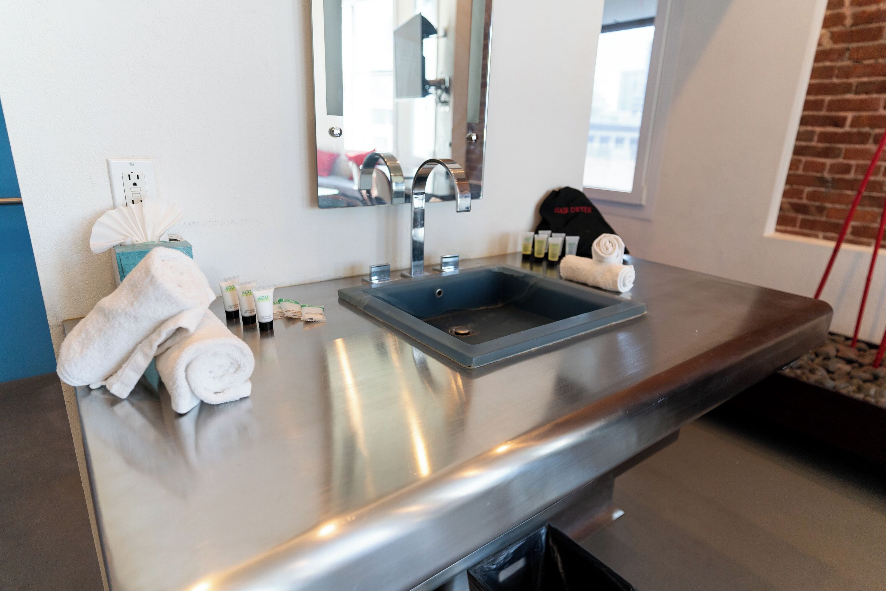 A modern bathroom with a stainless steel sink, a mirror, and toiletries on the counter.