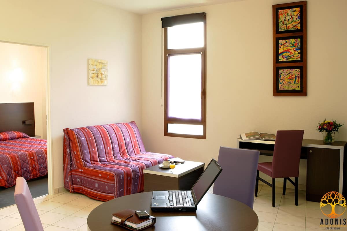 A hotel room with a bed, a sofa, a desk with a laptop, a chair, and a window.
