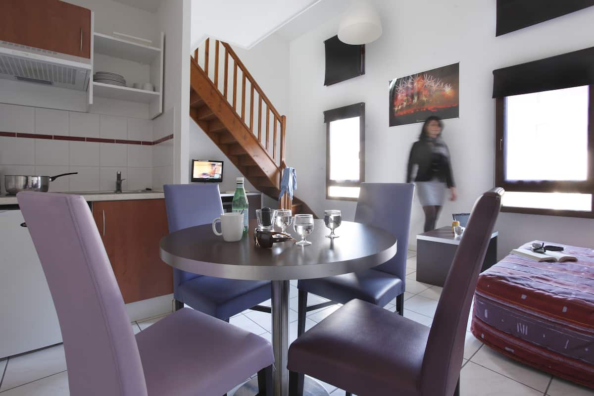 A modern kitchen with a dining area, a staircase, and a large window.