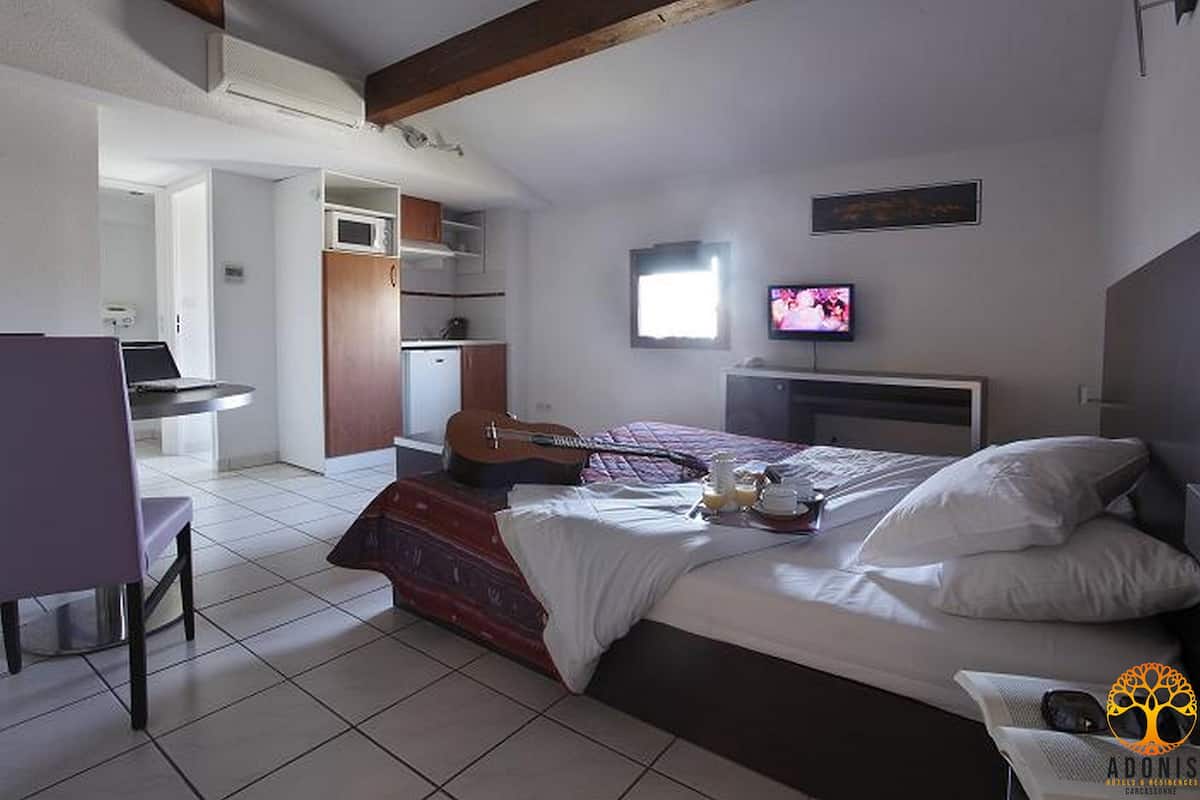 A bedroom with a bed, a guitar, a TV, and a desk with a chair.