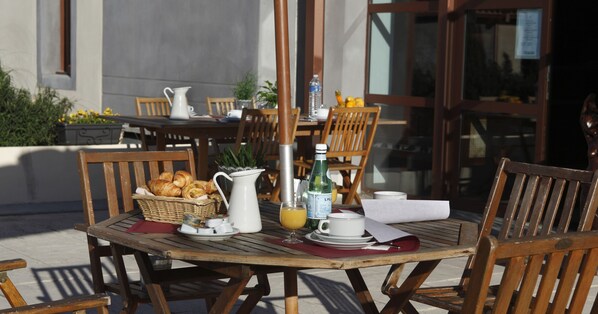 Une table en bois, dressée pour le petit-déjeuner, avec des croissants, un pichet, une bouteille de jus et des tasses.
