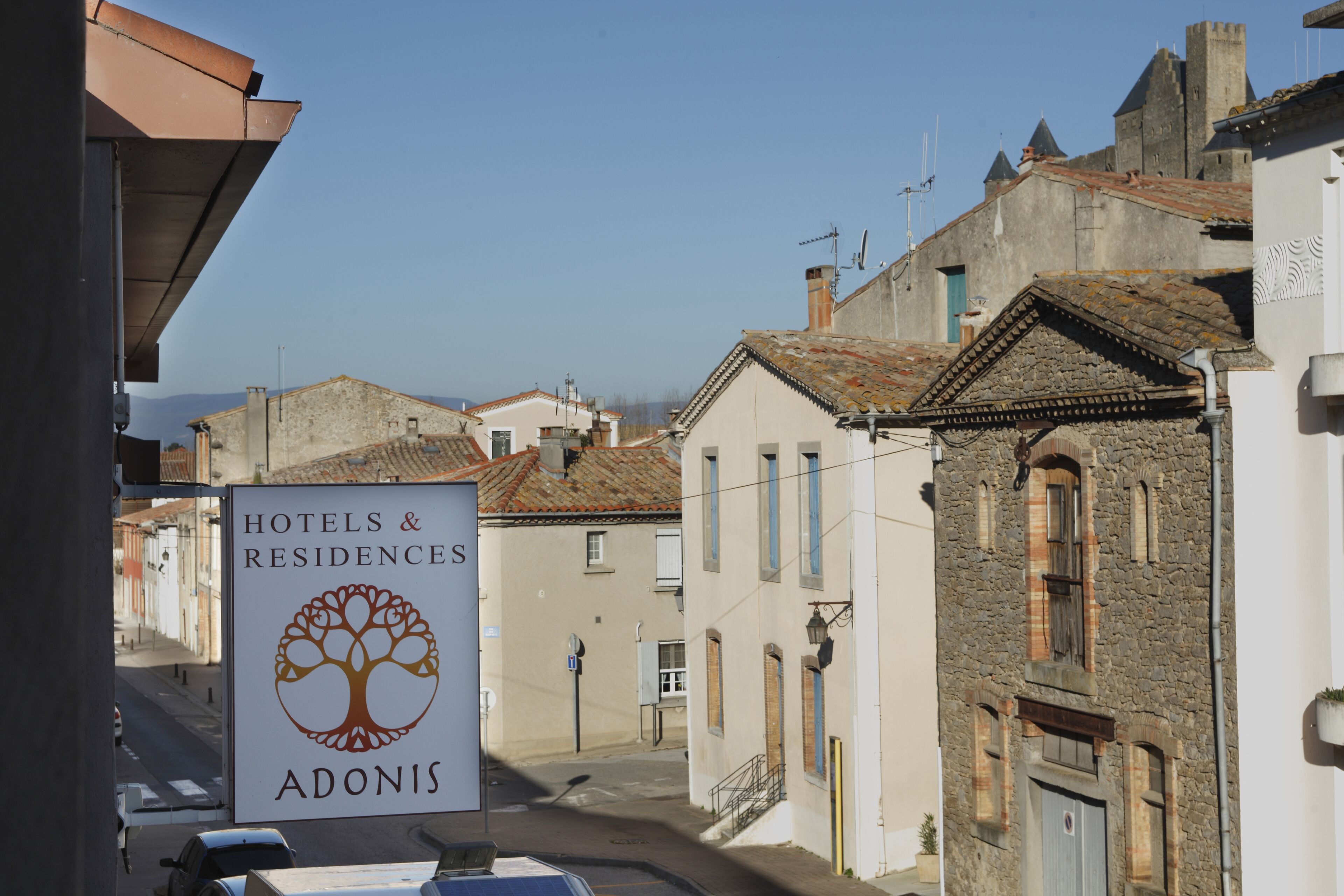 Een bord met 'HOTELS & RESIDENCES ADONIS', met een boomlogo, dat een hotel of residentie aangeeft.