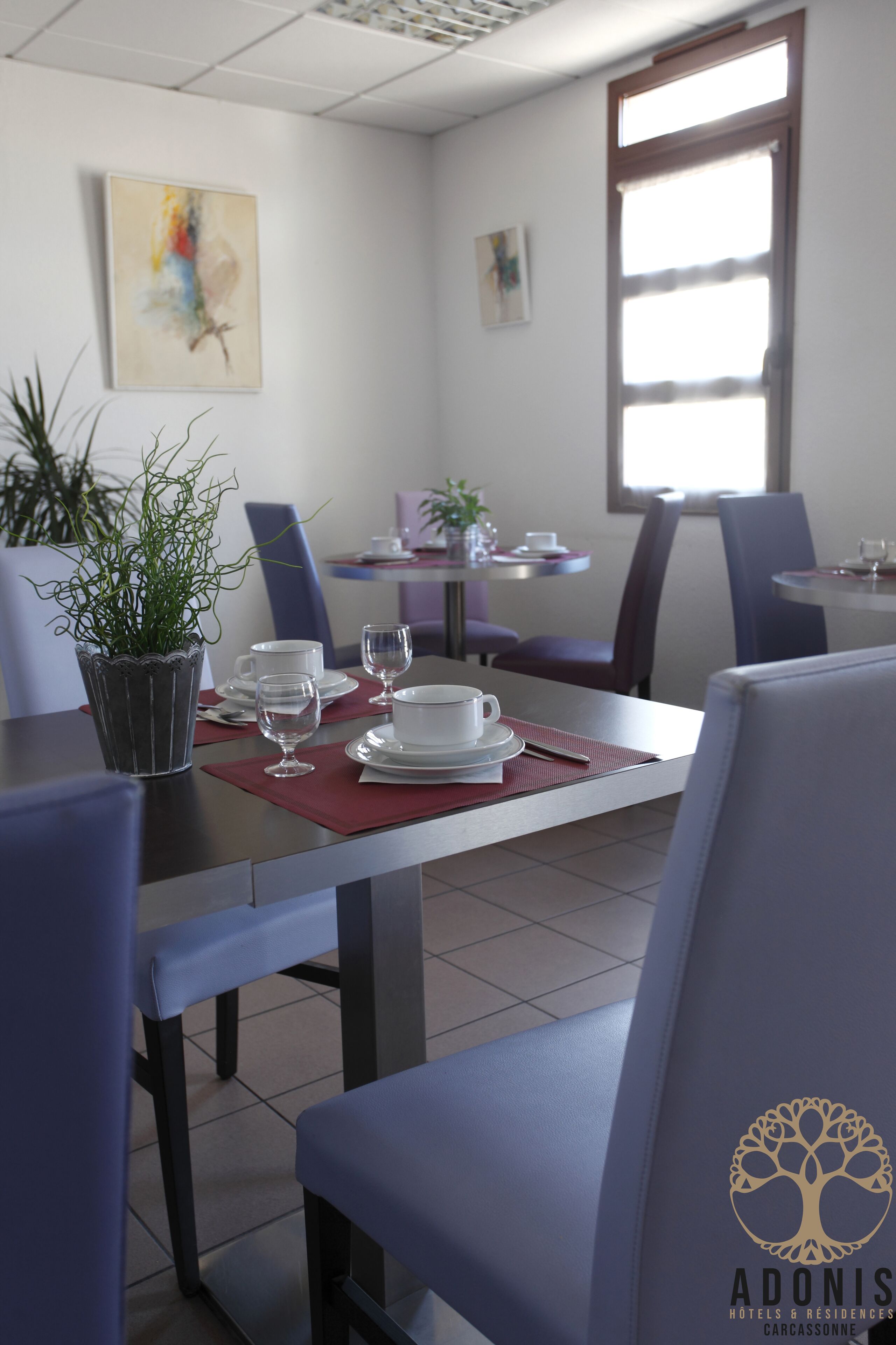 Zona pranzo con tavoli apparecchiati per due, sedie e una pianta in vaso.