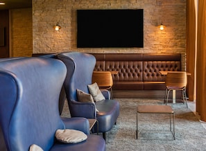 Un espace de détente moderne avec un mur en pierre, un grand téléviseur à écran plat, des fauteuils en cuir et deux tables en bois.
