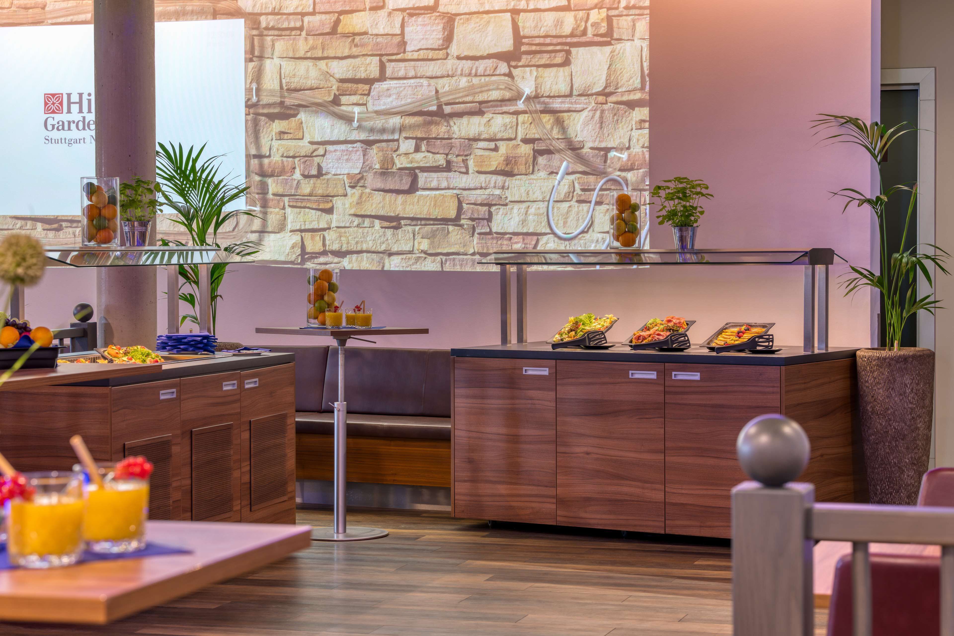Un moderno vestíbulo de hotel con una pared de piedra, un mostrador de recepción y una zona de buffet con diversos alimentos.