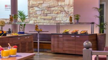 A modern hotel lobby with a stone wall, a reception desk, and a buffet area with various food items.