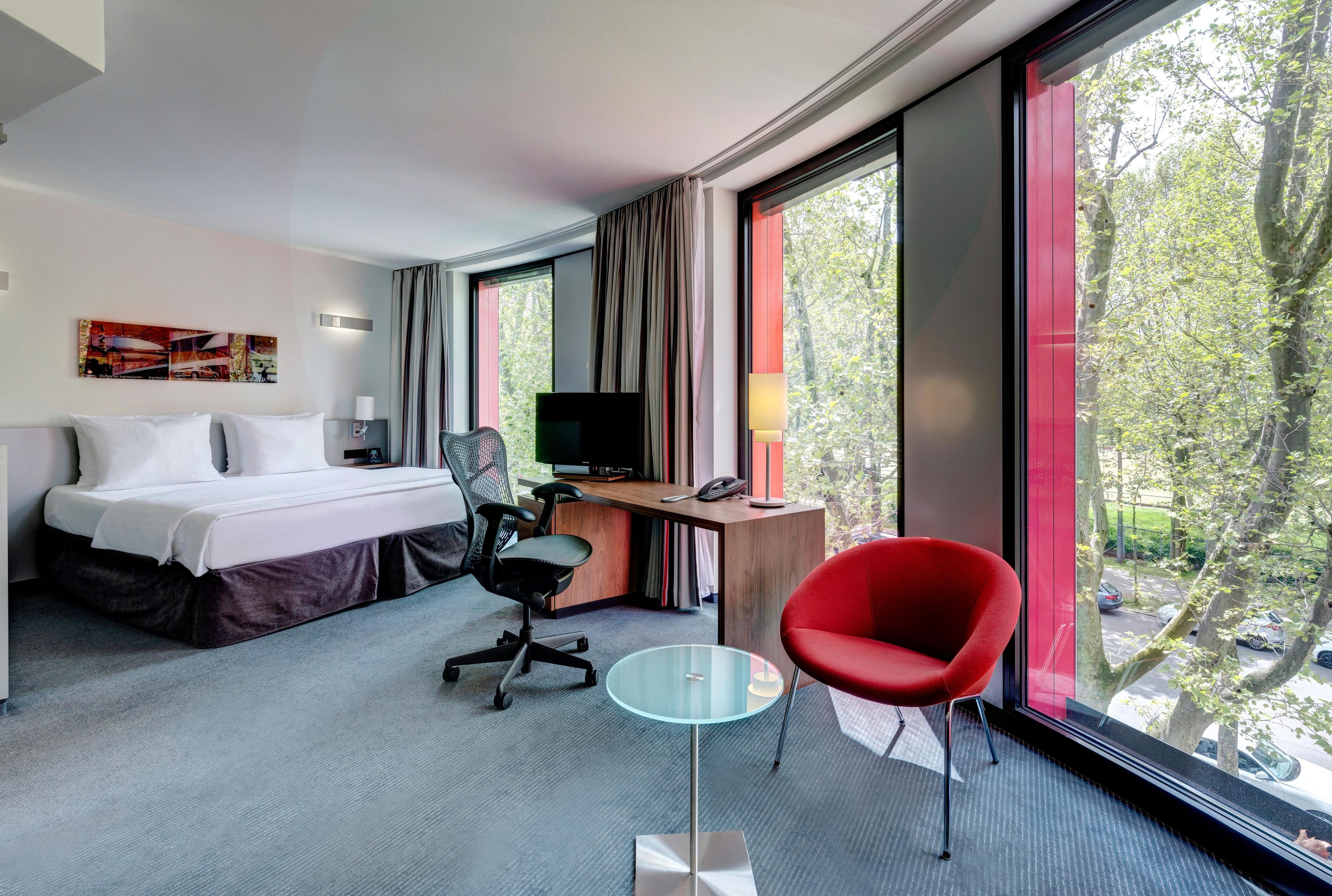 Habitación de hotel con cama, escritorio, silla, televisor y ventanas amplias.