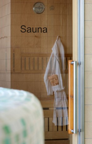 A sauna room with wooden walls, a visible clock, and a towel rack with a towel hanging on it. - Hilton Garden Inn Stuttgart Neckar Park (Stuttgart)