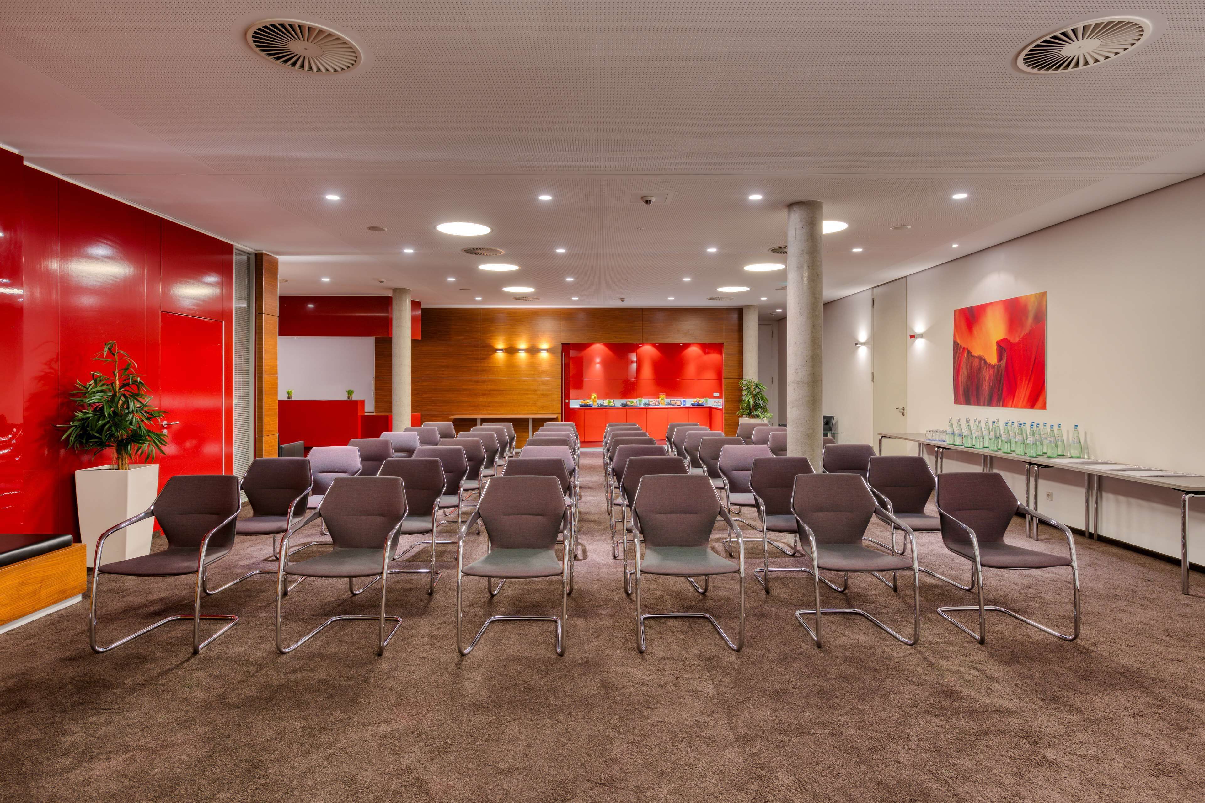 A conference room with rows of chairs, a stage with a red backdrop, and a large abstract painting on the wall.