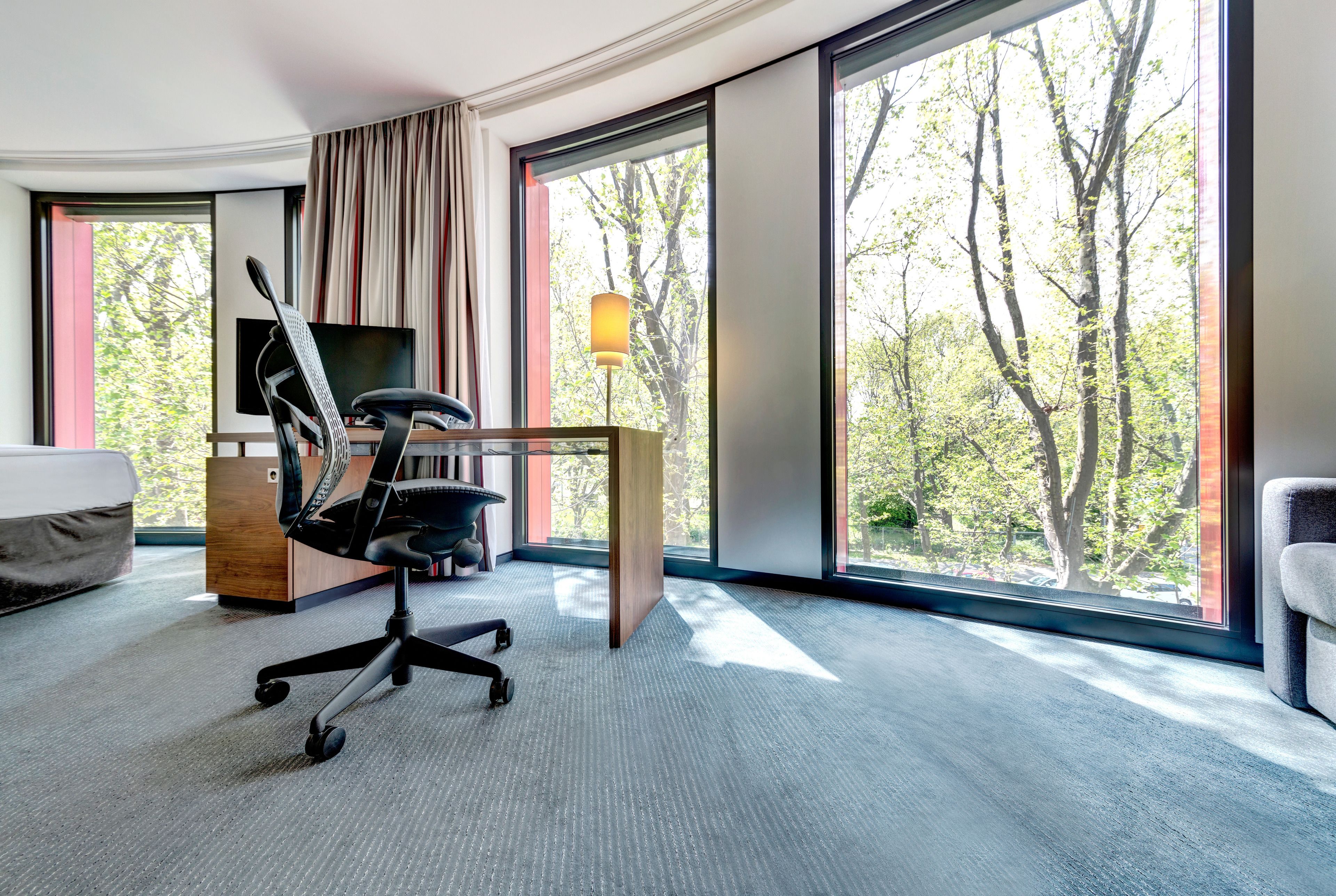 A hotel room with a large window, a desk, a chair, and a bed.