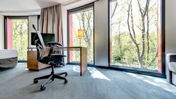 A hotel room with a large window, a desk, a chair, and a bed.