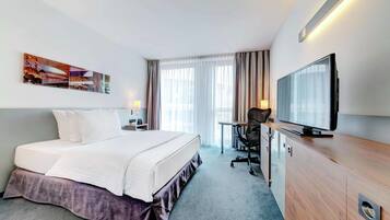 Une chambre d’hôtel avec un lit, un bureau et une chaise, une télévision et une grande fenêtre avec des rideaux.