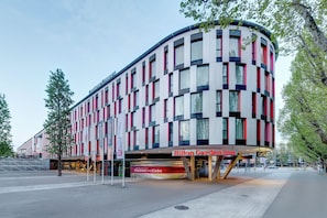 Un hôtel moderne à la façade incurvée, doté de nombreuses fenêtres et d’une entrée imposante.