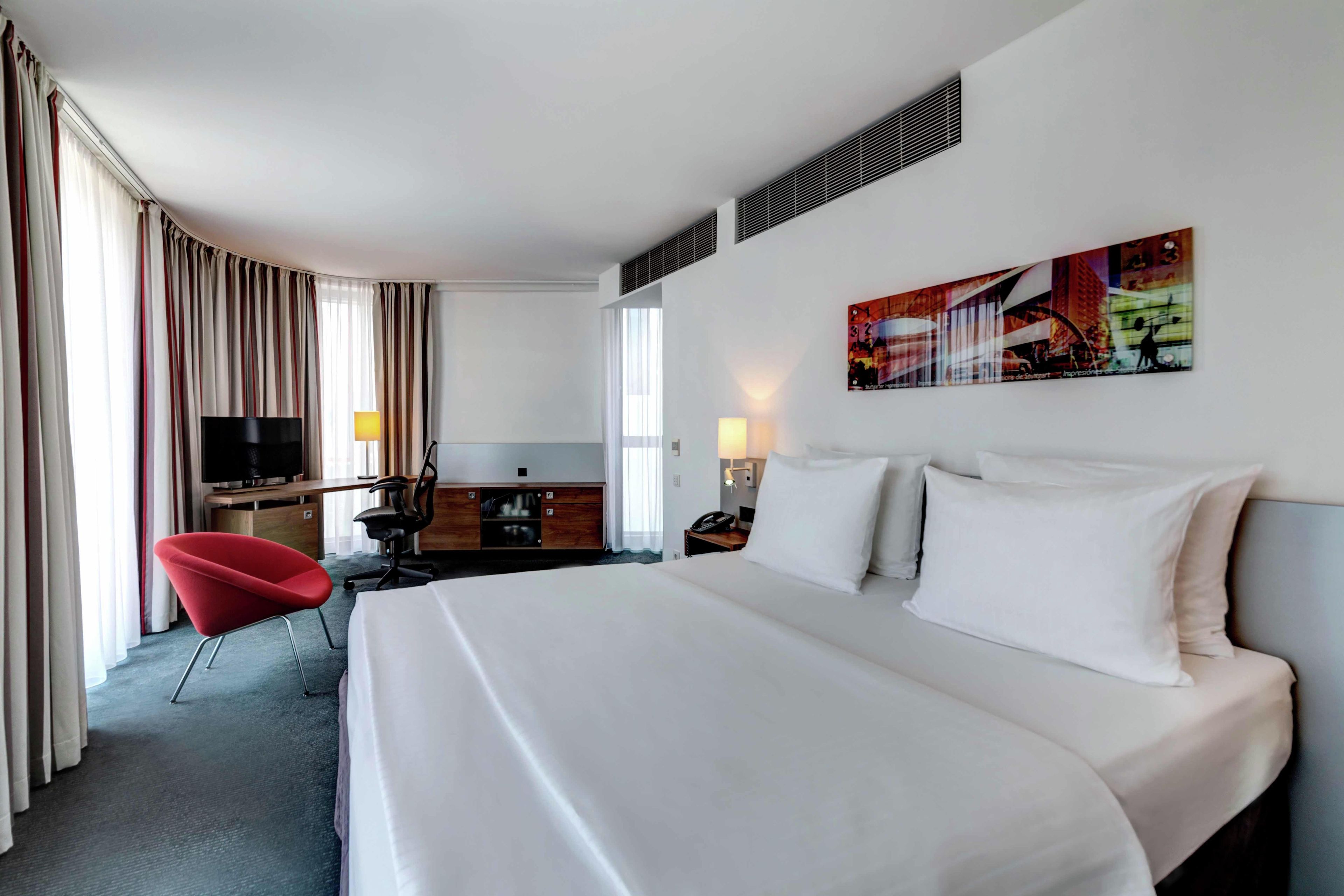 A hotel room with a large bed, a desk, a chair, a television, and a painting on the wall.