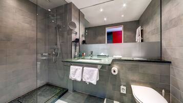 Un baño moderno con ducha de vidrio, lavamanos con espejo e inodoro.