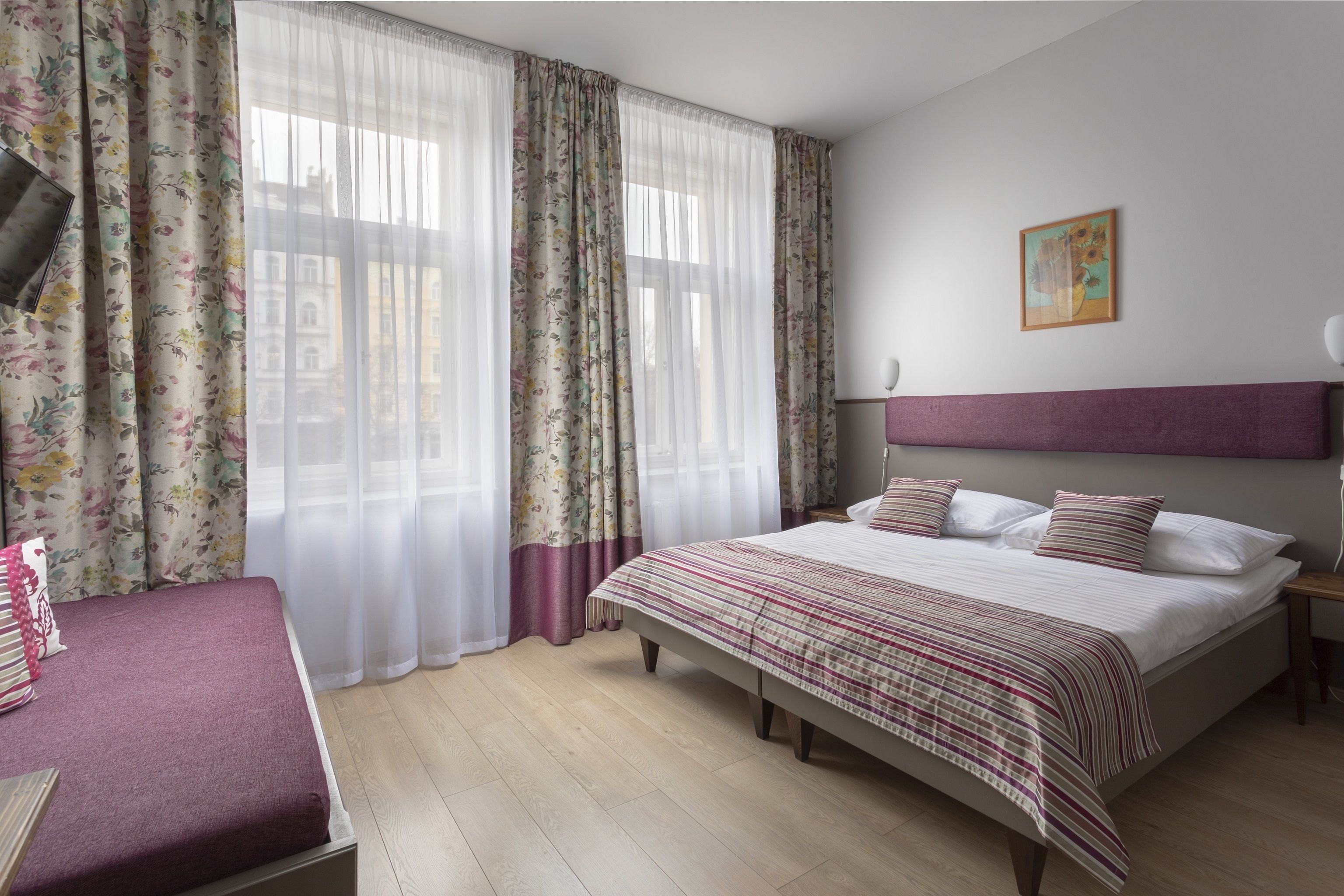 Un dormitorio con una cama grande, una mesita de noche, un televisor y una ventana con cortinas florales.