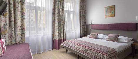 A bedroom with a large bed, a bedside table, a nightstand, a TV, and a window with floral curtains.