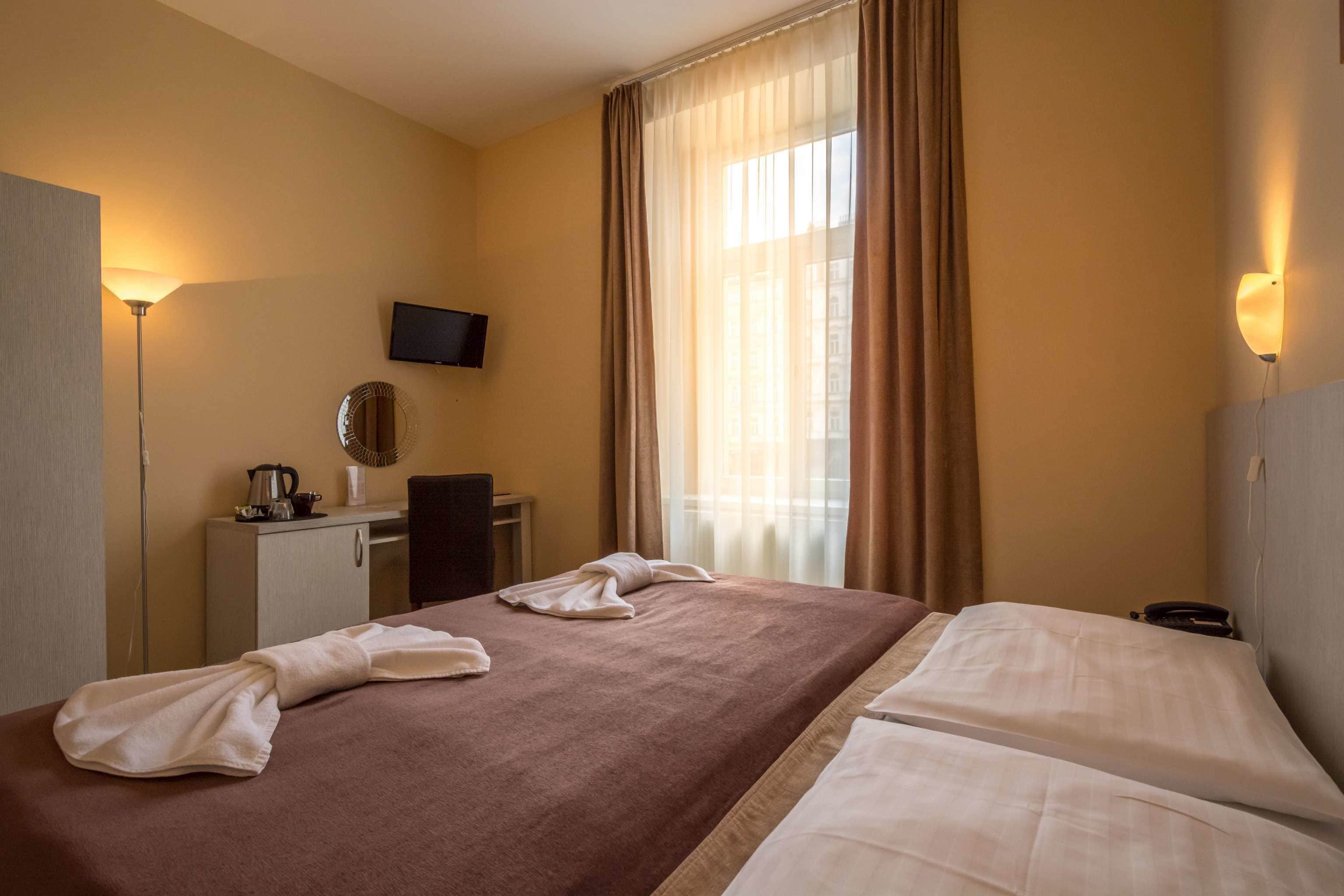 A hotel room with a bed, a desk, a chair, a television, and a window with curtains.